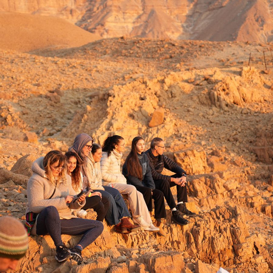 מטיילים יושבים על סלעי מדבר יהודה באור של שקיעה
